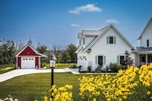 Ein zweistöckiges Haus mit roter Garage und weißem Hauptgebäude, umgeben von einer gepflegten Rasenfläche und gelben Blumen.