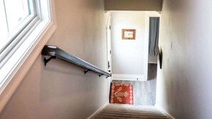 A staircase with a handrail, a window on the left, and a door at the top.