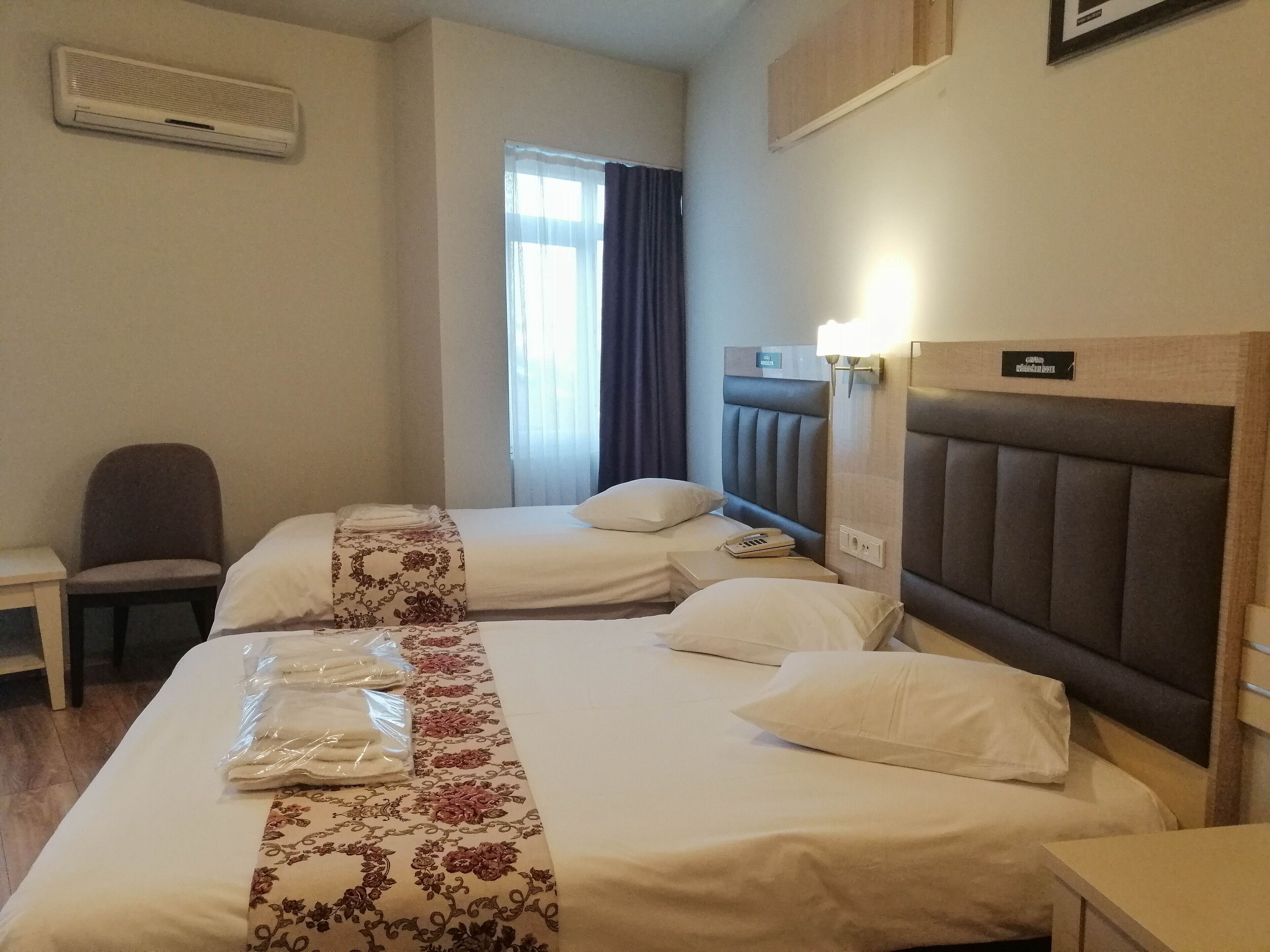 Quarto de hotel com duas camas, uma cadeira, uma escrivaninha e uma janela com cortinas.