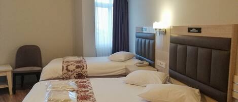 Quarto de hotel com duas camas, uma cadeira, uma escrivaninha e uma janela com cortinas.