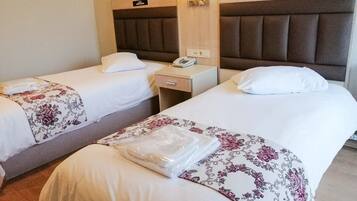 Una habitación de hotel con dos camas individuales, cada una con una almohada, una mesita de noche con una lámpara y un teléfono.