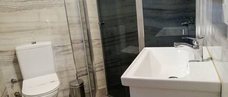 Un baño moderno con inodoro, cabina de ducha de vidrio y lavabo.