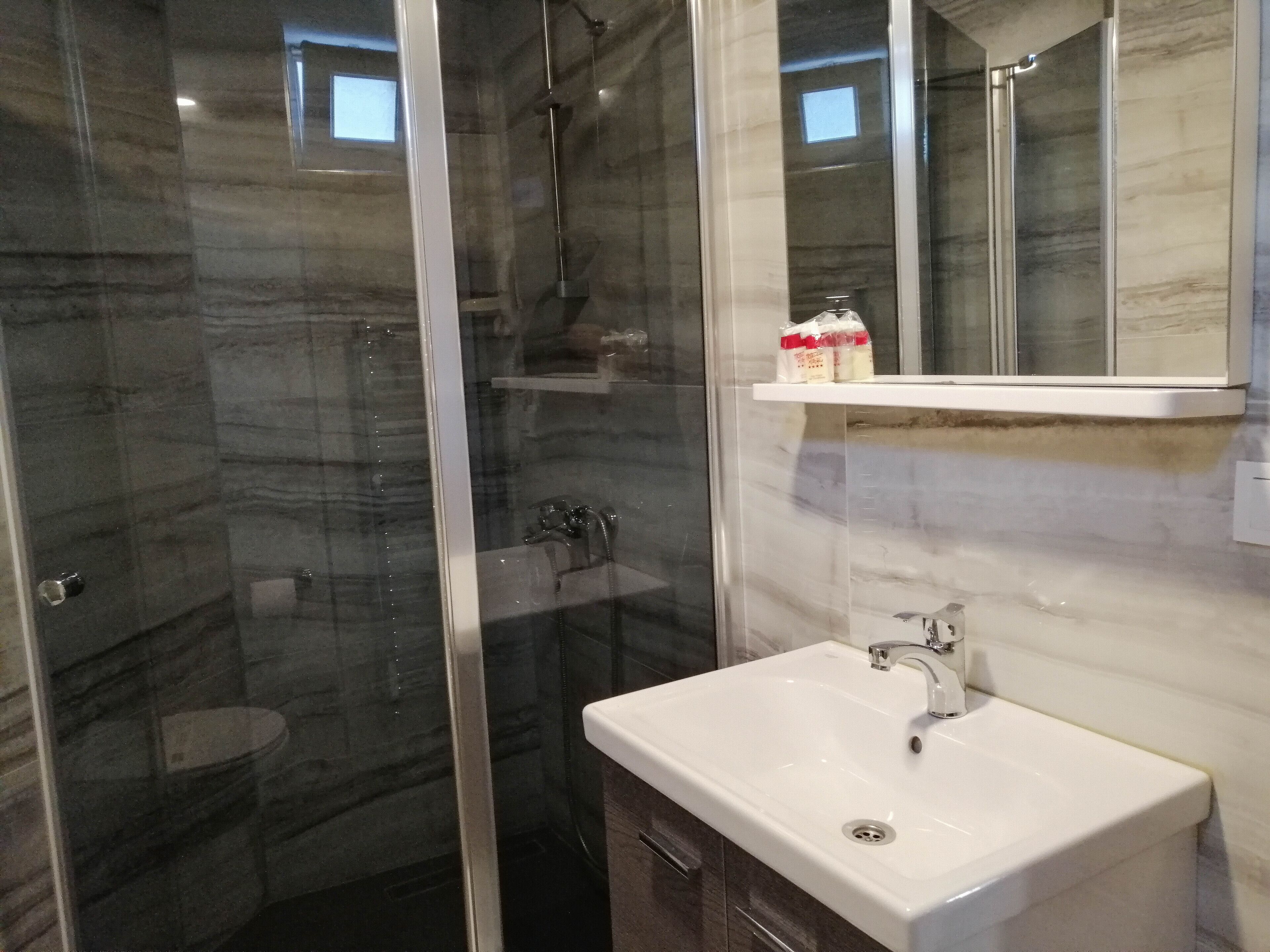 A modern bathroom with a glass-enclosed shower, a white sink, and a marble backsplash.