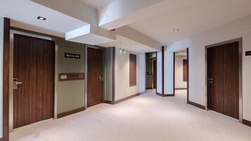 A modern hotel corridor with wooden doors, numbered room signs, and recessed ceiling lighting.