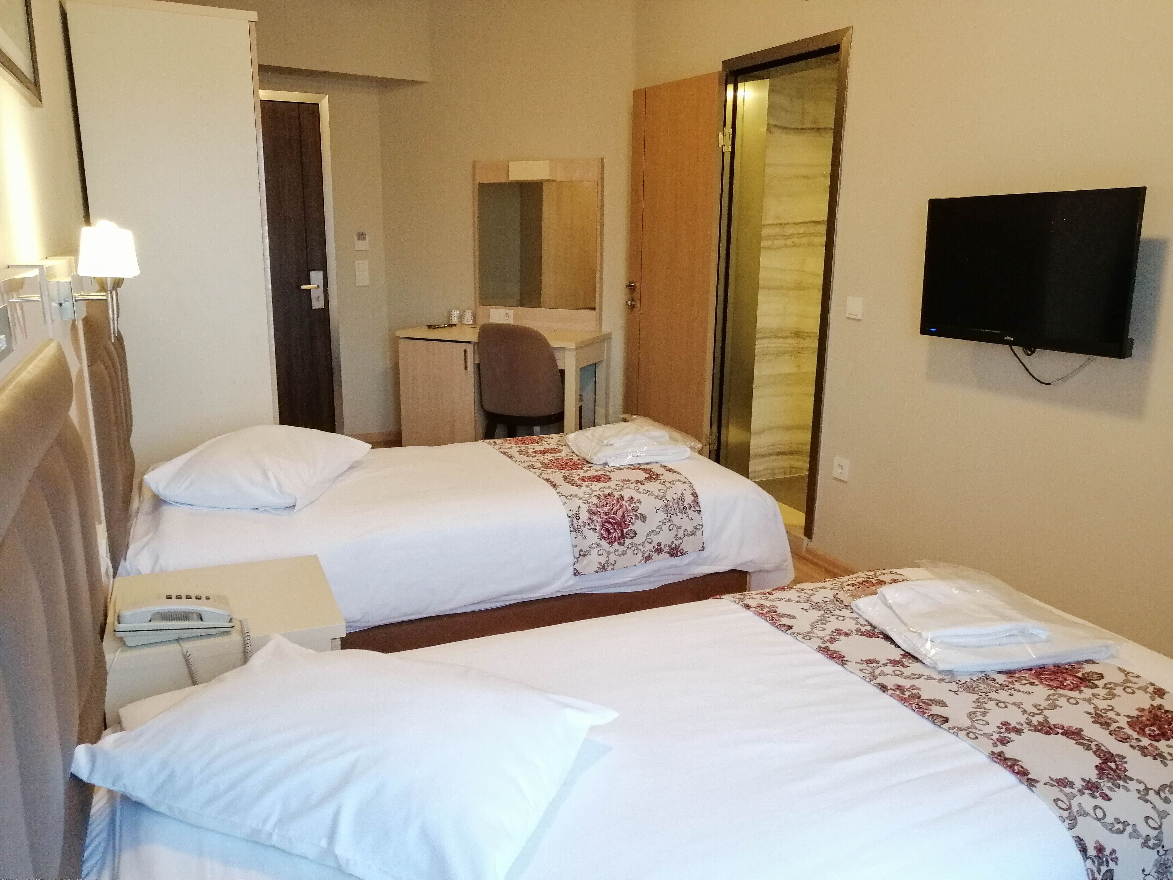 A hotel room with two beds, a desk, a chair, a TV, and a bathroom door.