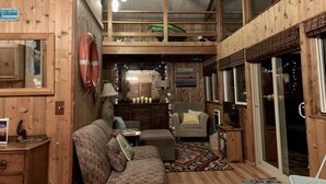 Un acogedor interior de cabaña con detalles de madera, un sofá, una silla, una mesita y un televisor.