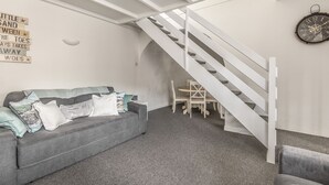 A modern interior with a grey sofa, a staircase, and a wall clock. - Cottage - Sleeps 6 - Pet Friendly - Patio (St Austell)