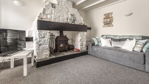 A cozy living room with a stone fireplace, a grey sofa, and a flat-screen TV. - Cottage - Sleeps 6 - Pet Friendly - Patio (St Austell)