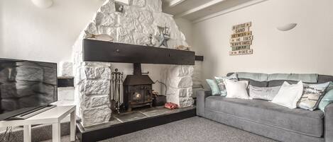 Una sala de estar acogedora con chimenea de piedra, un sofá gris y un televisor de pantalla plana.