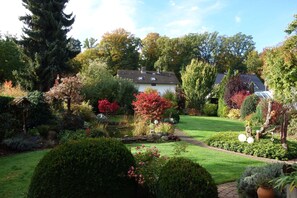 Un jardin bien entretenu, avec une grande variété de plantes et un bassin, une maison avec un toit en tuiles et un ciel dégagé.