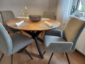 Une table de salle à manger ronde en bois, agrémentée d’un centre de table en fibres tressées, entourée de six chaises grises à revêtement en tissu et à pieds noirs.