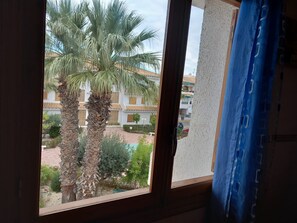 A window with a view of palm trees and a building with a tiled roof. - Beach Vacation in Tamarit (Santa Pola)