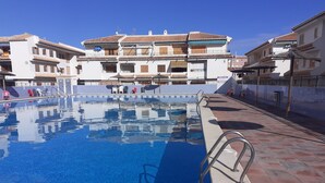 A swimming pool with a clear blue water surface, surrounded by a tiled deck and a row of buildings with balconies. - Holidays in Tamarit beach  (Santa Pola)