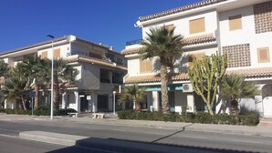 A street view with two-story buildings, palm trees, and a clear blue sky. - Holidays in Tamarit beach  (Santa Pola)
