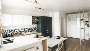 Une cuisine moderne avec des armoires blanches, un pare-feu noir et blanc et un plan de travail en bois. On y trouve une table à manger avec des chaises, un radiateur sous le plan de travail et une plante posée sur le plan de travail.