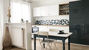 Une cuisine compacte avec des meubles blancs, un plan de travail noir et un coin repas comprenant une table et des chaises.