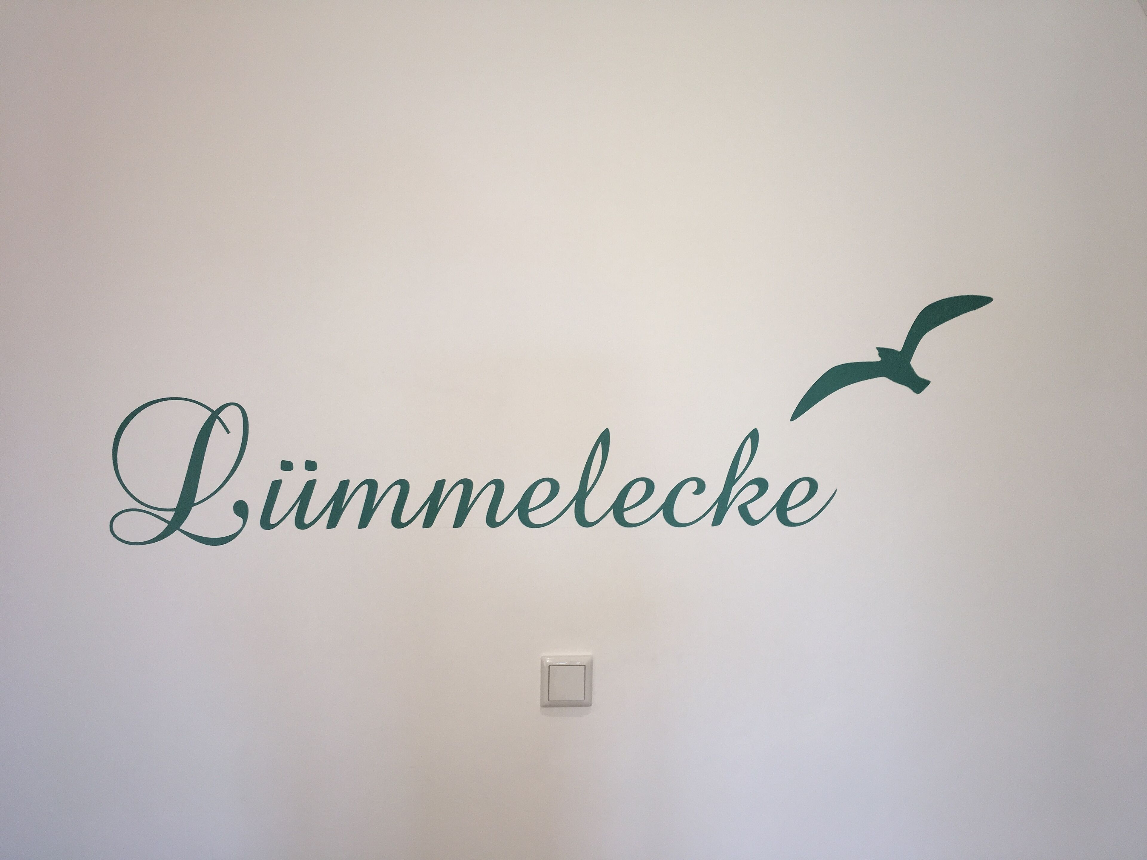 Seinässä on tekstiä, jossa lukee ”Lümmelecke”, ja sen lisäksi seinässä on linnun siluetti.