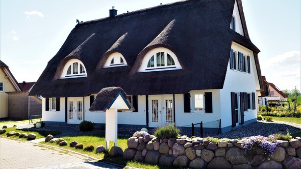 Ett traditionellt hus med ett brant tak, flera skorstenar och en välskött trädgård med en stenmur och blommande växter.