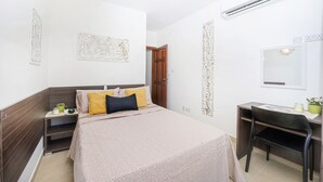 Ein Schlafzimmer mit Bett, Nachttisch, Schreibtisch, Stuhl und einer Klimaanlage.