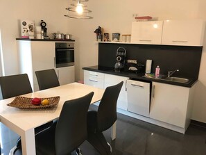 Una cocina moderna con gabinetes blancos, encimera negra y un comedor con mesa y sillas negras.