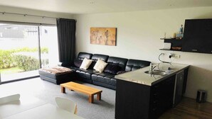 Un salon moderne avec un canapé en cuir noir, une table basse en bois et une table à manger blanche. Il y a également un coin cuisine avec un évier et des placards.