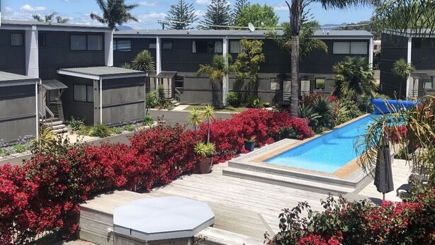 Un hôtel moderne doté d’une piscine, entouré d’une végétation luxuriante, de fleurs rouges éclatantes et de palmiers.
