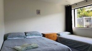 Une chambre avec deux lits, une commode en bois et une fenêtre donnant sur un paysage verdoyant et des bâtiments.