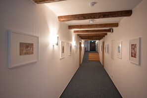 Un couloir aux murs ornés de tableaux encadrés, avec des poutres en bois au plafond et un sol recouvert de moquette.