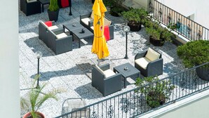 Una terraza en la azotea con mesas al aire libre, plantas en macetas y un paraguas amarillo.