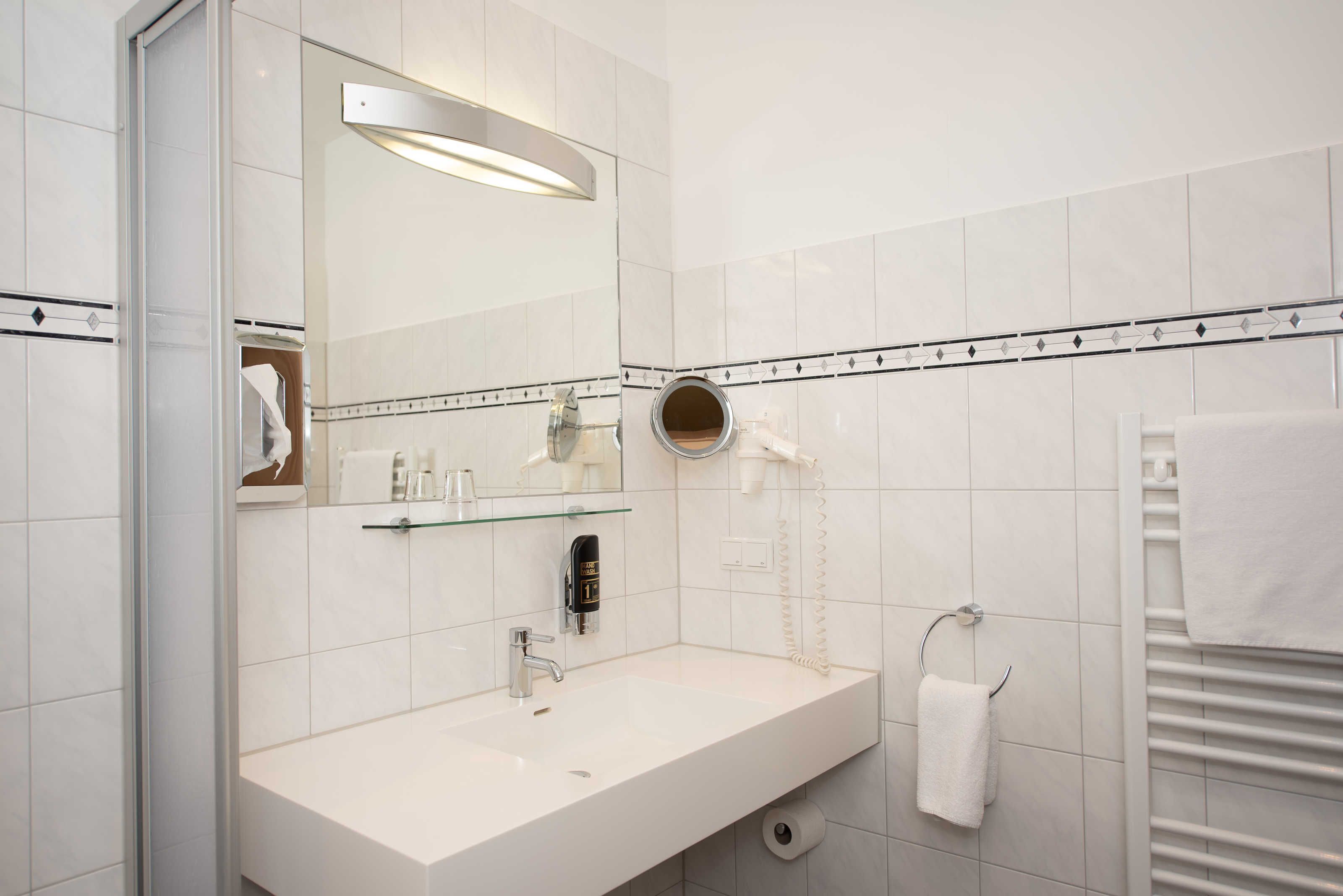 Un bagno moderno con un lavandino bianco, uno specchio, un asciugacapelli e un porta asciugamani.