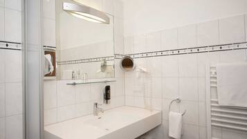 Un bagno moderno con un lavandino bianco, uno specchio, un asciugacapelli e un porta asciugamani.