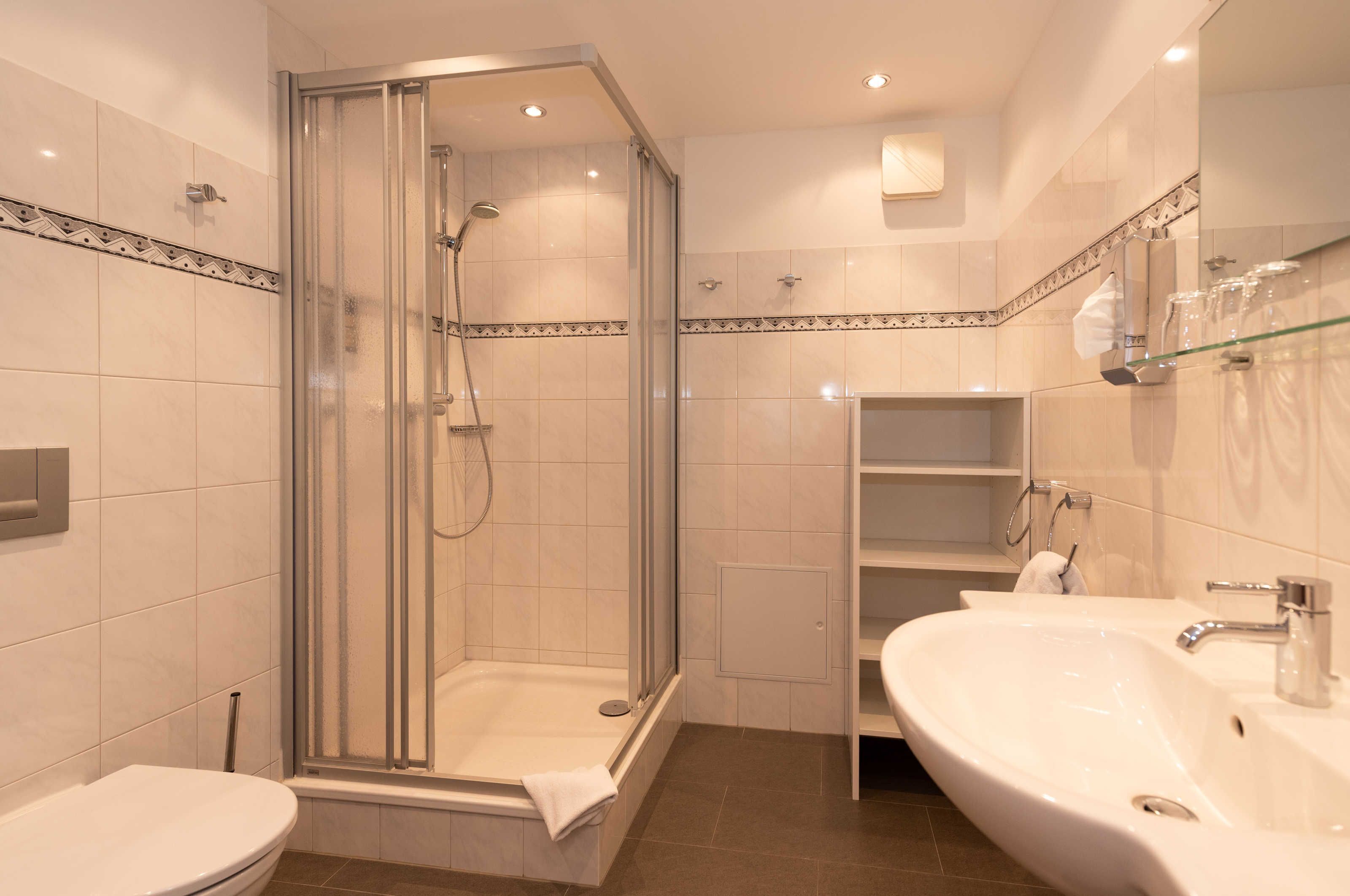 Ein modernes Badezimmer mit einer gläsernen Duschkabine, einem weißen Waschbecken und einem gefliesten Boden.