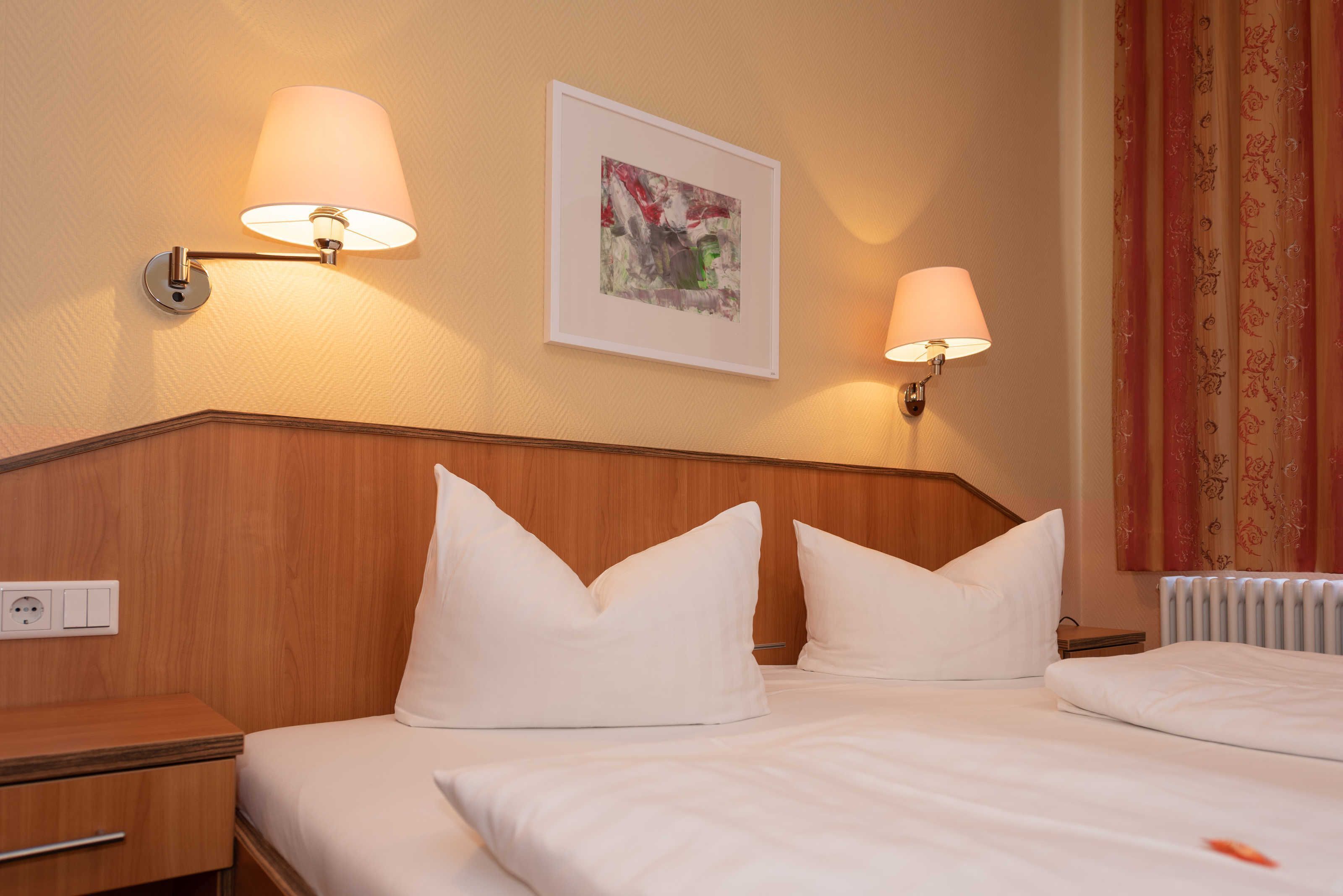 Een hotelkamer met twee bedden, een houten hoofdbord, een lijst met een foto aan de muur en twee wandlampen.
