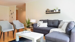 A living room with a grey sofa, two armchairs, a white coffee table, and a small side table with a lamp and decorative items. - Machico Beach, a Home in Madeira (Machico)