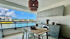 A modern kitchen with grey cabinets, a dining table with two white chairs, and a view of the sea and buildings through large windows. - Studio in the heart of Saint François on the Marina (Saint francois)