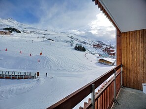 A snow-covered ski slope with a wooden building and a balcony overlooking the area.