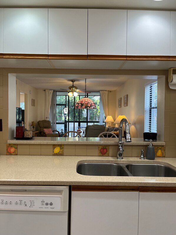 Cozinha com lava-louças, pia e janela com cortinas.