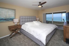 A bedroom with a large bed, a ceiling fan, a painting, a nightstand, a lamp, a TV, and a view of the ocean through a sliding door. - Horizons West #605 - Panoramic View on the #1 Beach (Sarasota)
