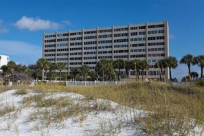 A multi-story building with a flat roof, surrounded by sand dunes and palm trees. - Horizons West #605 - Panoramic View on the #1 Beach (Sarasota)