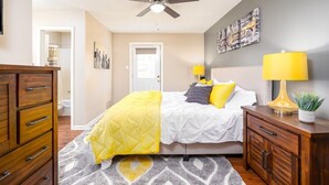 Une chambre à coucher avec un lit, un ventilateur de plafond, une table de chevet, une commode et une porte.