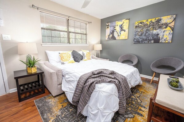 A bedroom with a bed, bedside tables, a lamp, a chair, and artwork on the wall.
