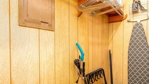 Quarto com painéis de madeira, um respiradouro no teto, um cabide com toalhas, um aspirador de pó e uma toalha estampada na parede.