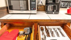 Cozinha compacta com micro-ondas, cafeteira e gaveta com utensílios de cozinha.