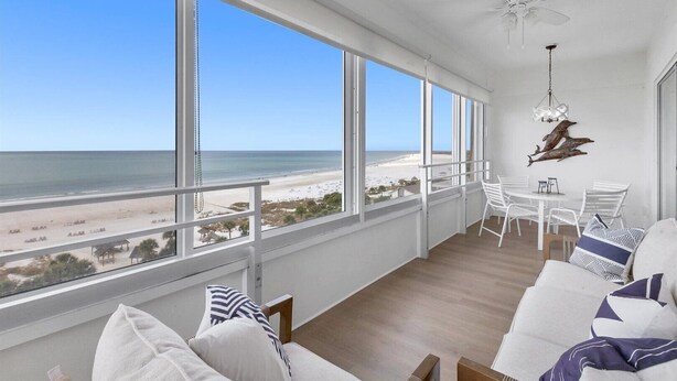 Un balcon avec vue sur la plage, des meubles blancs et un ventilateur de plafond.