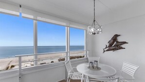 Une pièce dotée d’une grande fenêtre donnant sur une plage, d’une table ronde entourée de chaises et d’un élément décoratif mural.