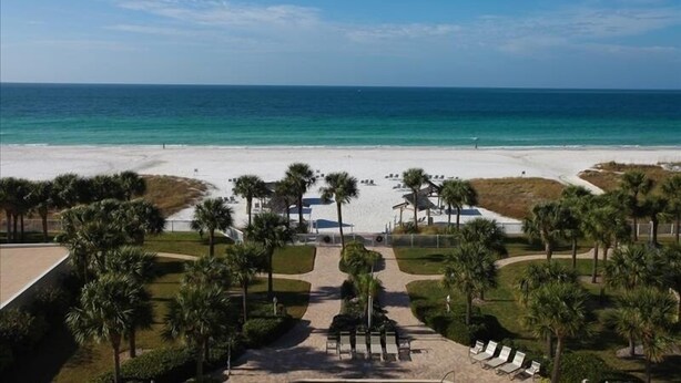 A beach resort with a clear view of the ocean, palm trees, and a pathway leading to beach chairs.