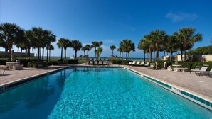 A clear blue pool with lounge chairs and palm trees, surrounded by a paved deck.