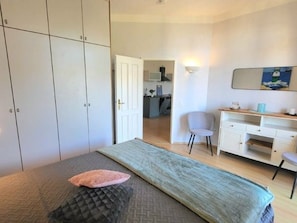 A bedroom with a bed, a desk, and a chair. There is a door leading to a kitchen area. - (63) 2-room apartment Ostseeallee - Apartment house Sonnenresidenz I (Kühlungsborn)