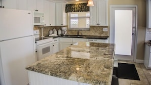 A kitchen with white cabinets, a granite countertop, a microwave, a stove, and a sink. - Horizons West Villa A-11 - on Siesta Key's #1 Beach (Sarasota)