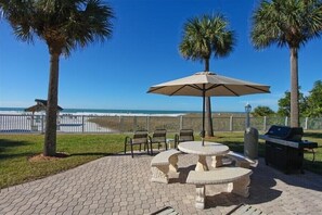 Une terrasse extérieure avec une table et des chaises, un barbecue et une vue sur la plage.